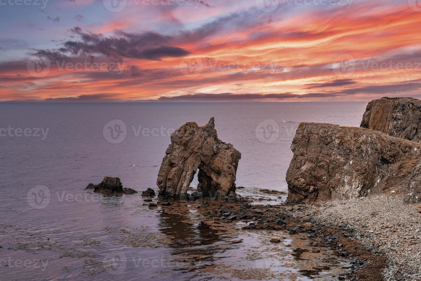 Scenic view of rock formations at seashore against dramatic sky during sunset photo