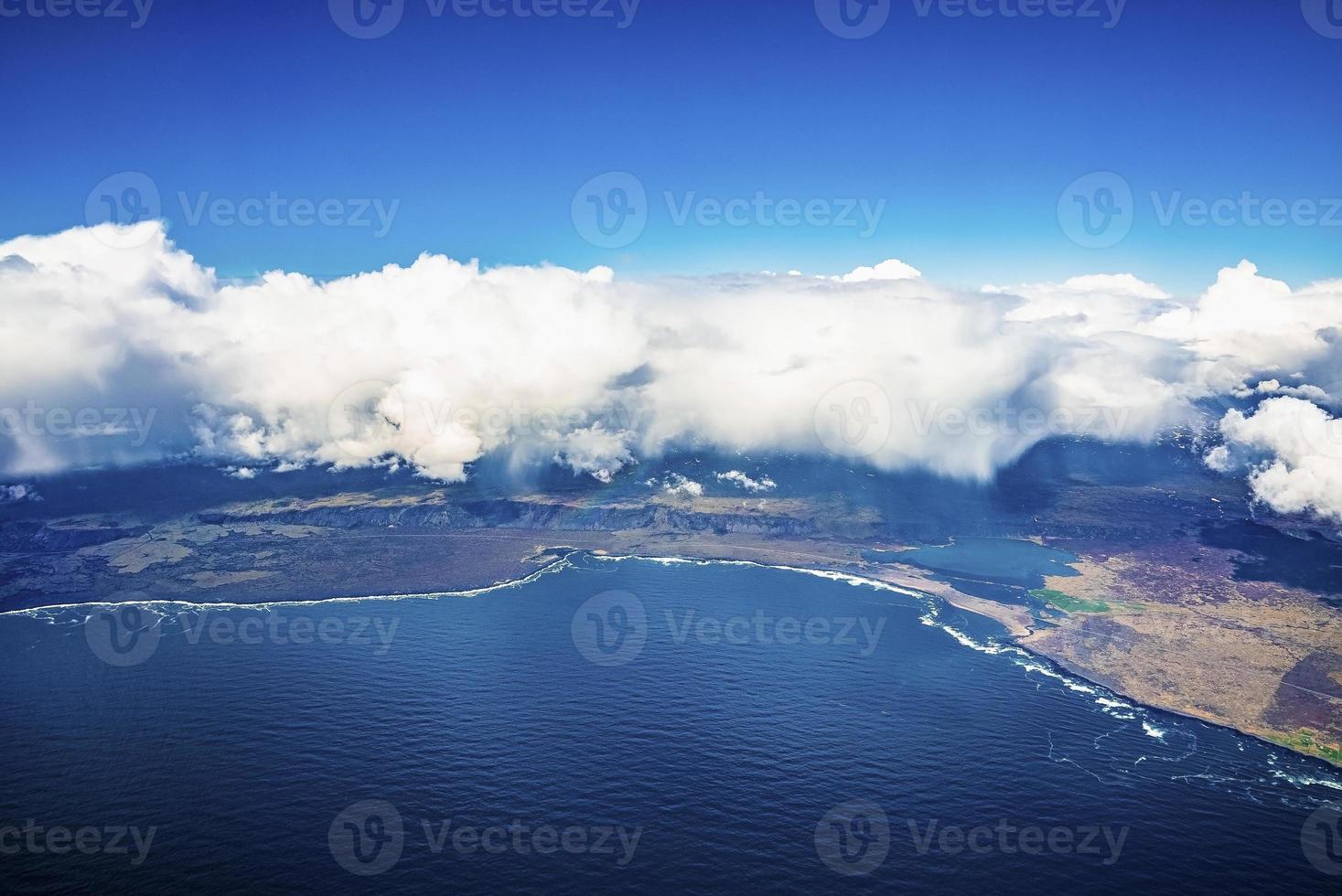 Beautiful view of clouds covering landscape by seaside against blue sky photo