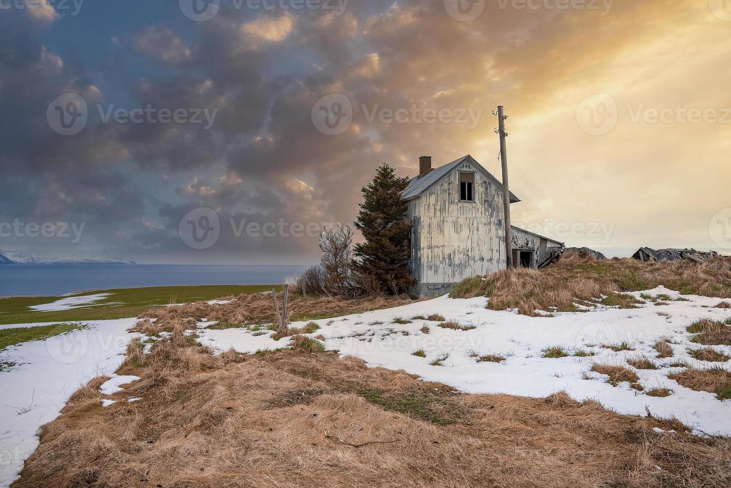 Wooden house on snow covered landscape against cloudy sky during sunset photo