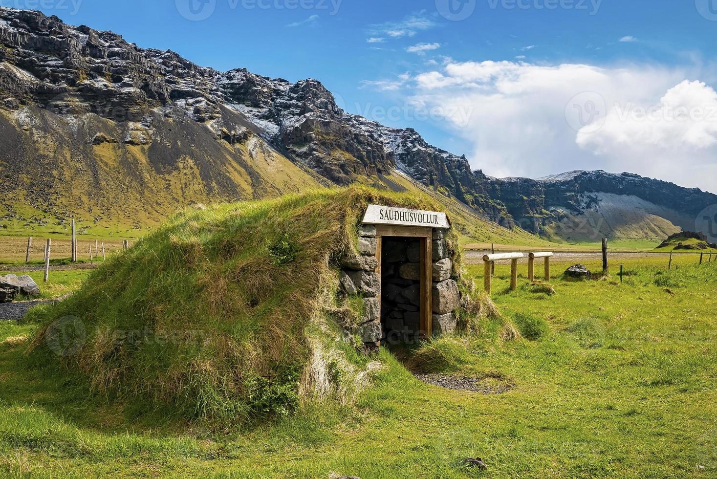 Beautiful Saudhusvollur turf shelter by mountain against blue sky photo