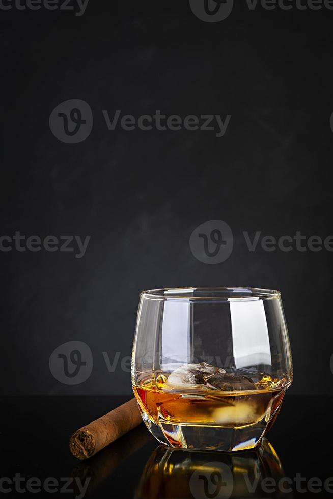 Glass of whiskey and cigar on dark background. photo