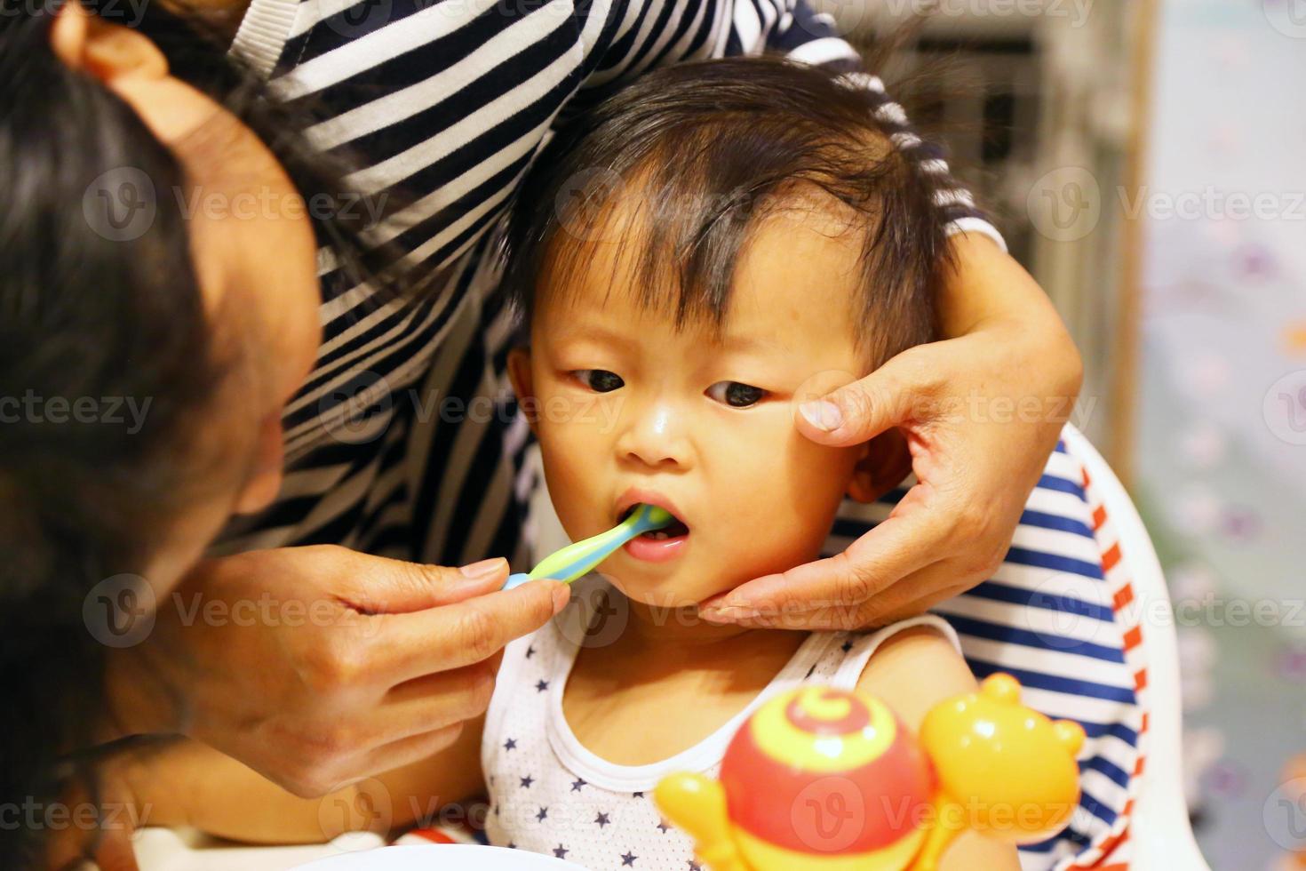 retrato de madre enseñando a un lindo bebé a cepillarse los dientes con cepillo de dientes. niño asiático con madre. foto