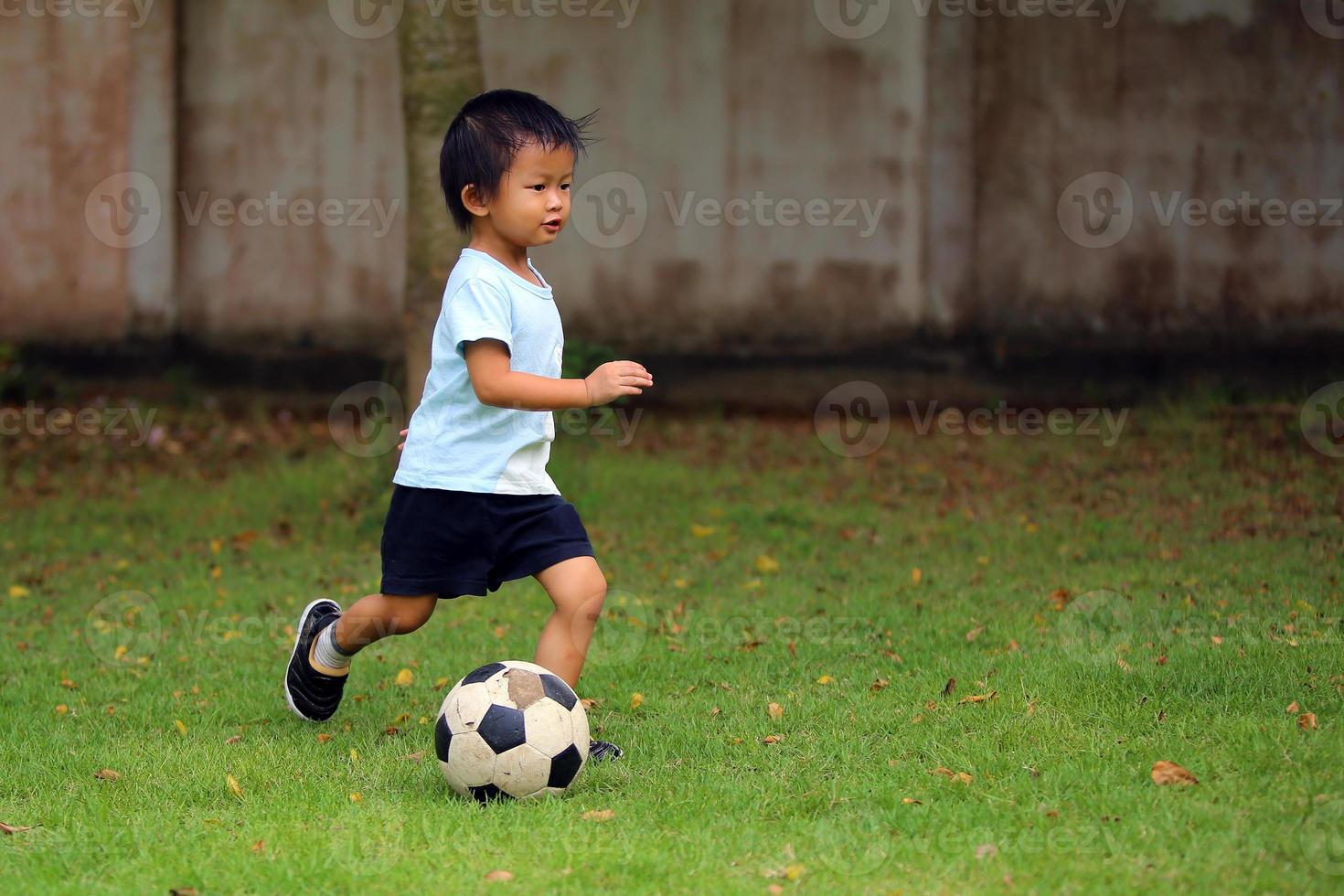 Asian boy playing football in the park. Kid dribbling ball in grass field. photo