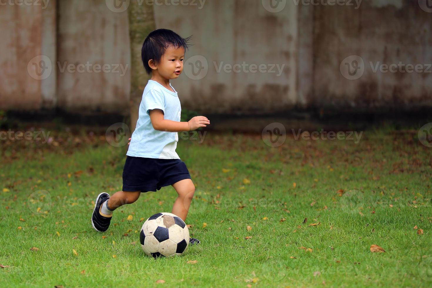 niño asiático jugando al fútbol en el parque. niño regateando la pelota en el campo de hierba. foto