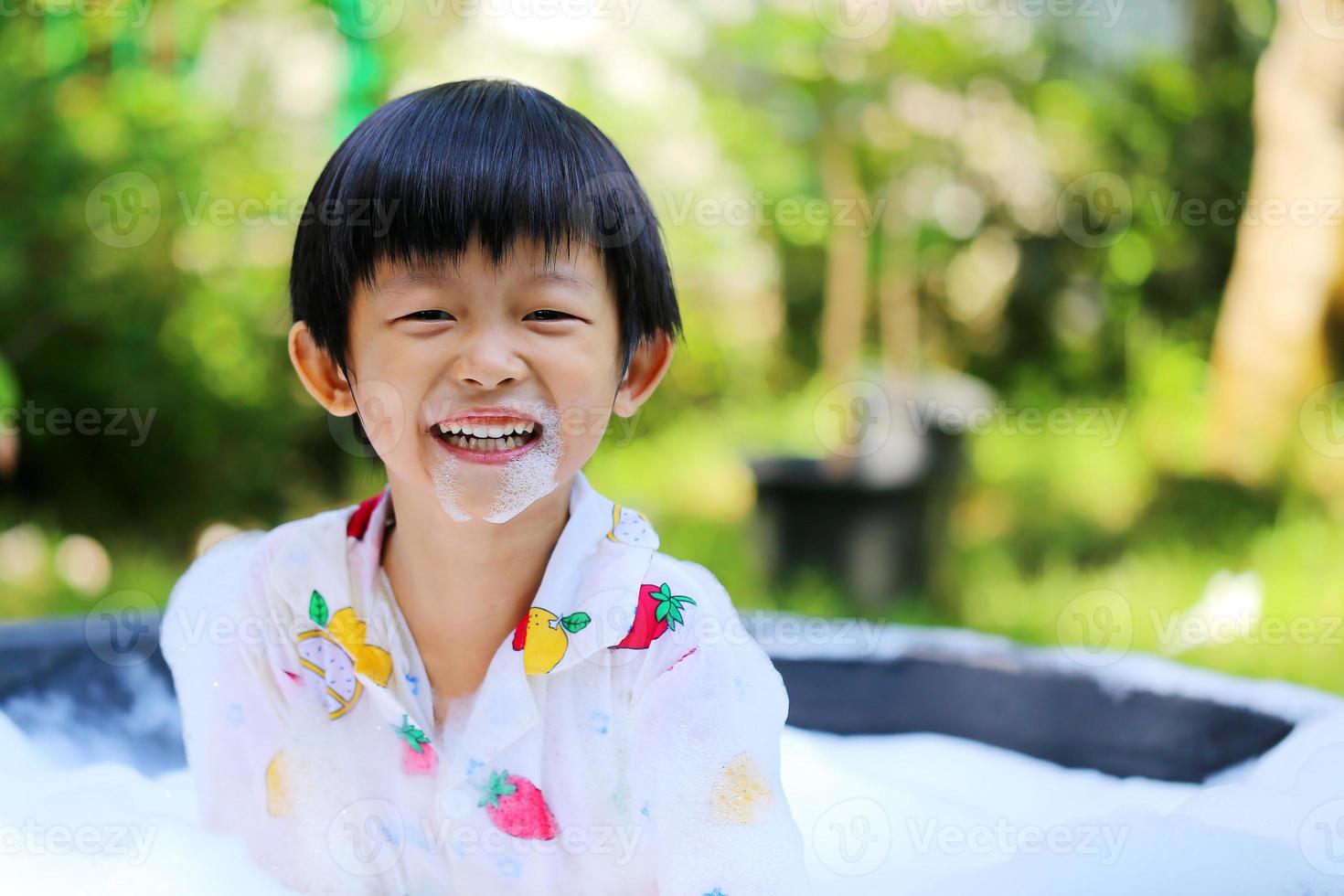 Asian boy smiling and playing bubble foam in basin at backyard in sunshine day, Happy boy make splashing water photo