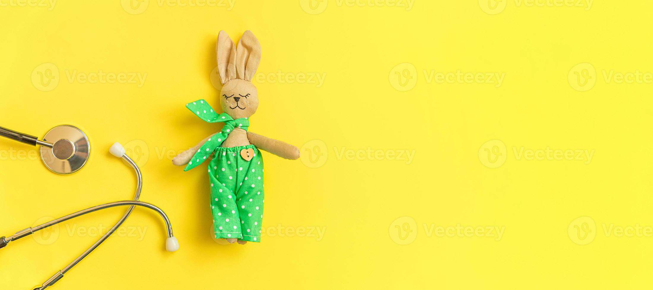Simply minimal design toy bunny and medicine equipment stethoscope isolated on yellow background. Health care children doctor concept. Pediatrician symbol. Flat lay top view layout, copy space banner photo