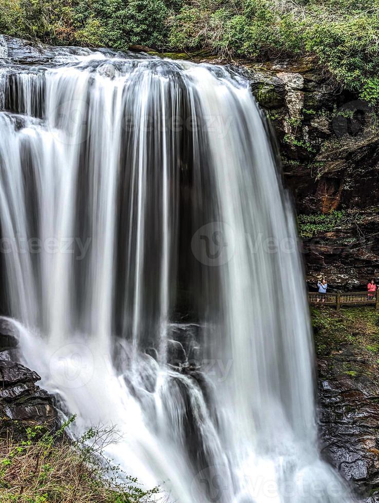 A scenic waterfall roadside going over the cliff down to the boulders and rocks below where you can no longer drive under but can walk underneath the raging waters photo