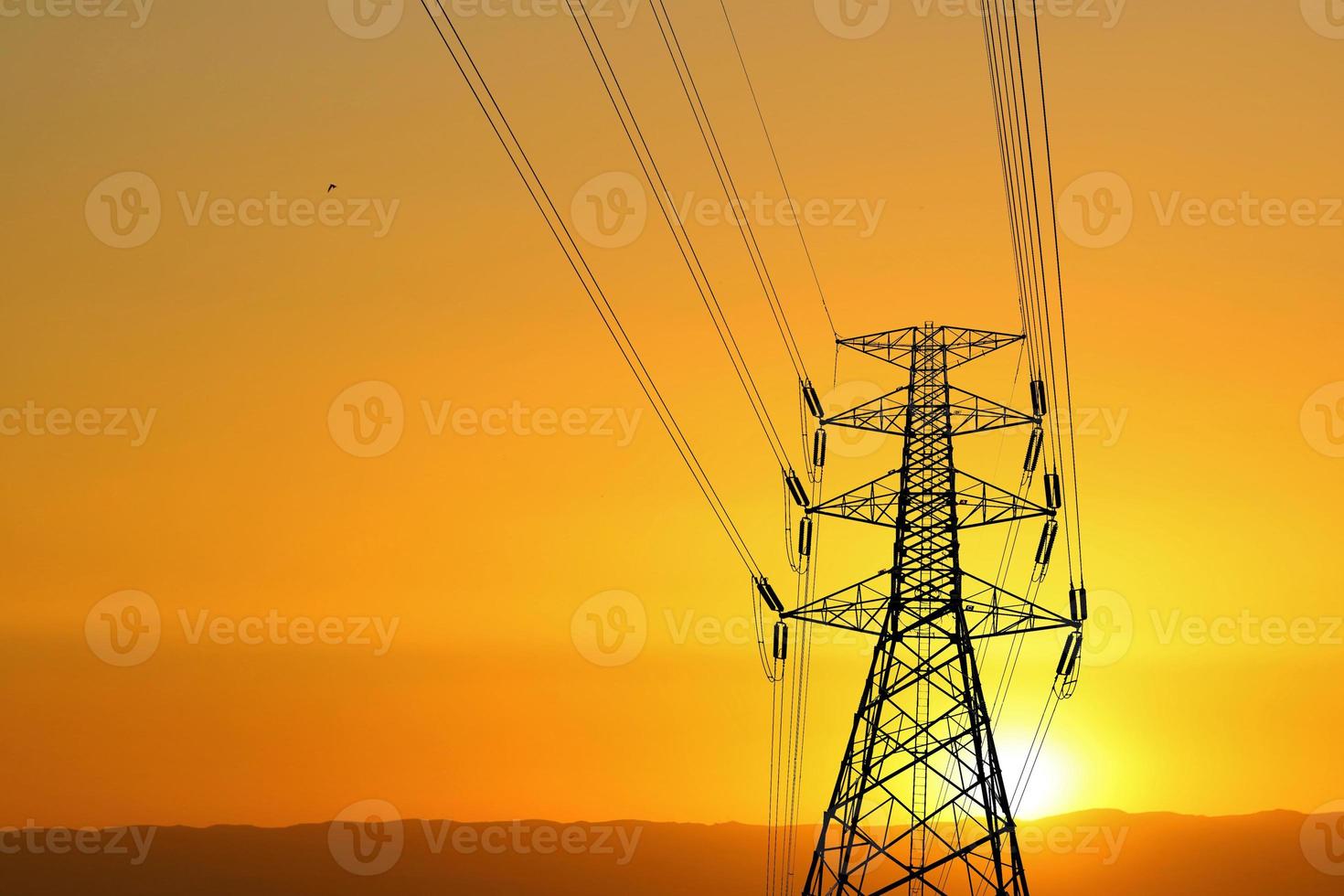 Silhouette of high voltage poles with electric wires. Silhouette of high voltage power line cables in an orange evening sunset. Steel structure of electric poles. electric power transmission concept photo