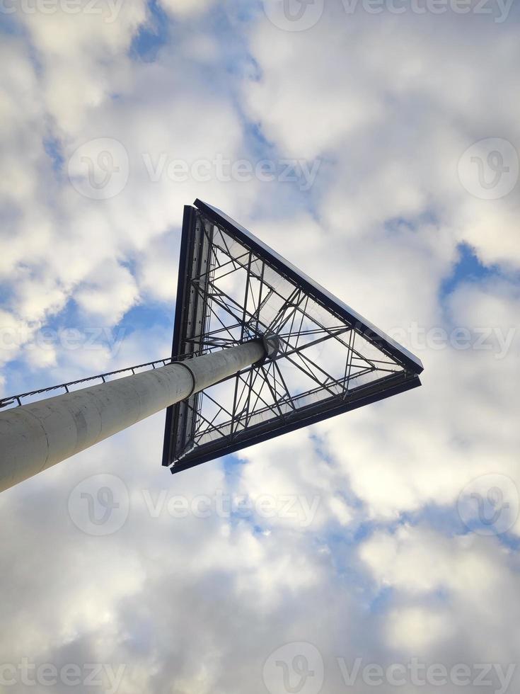 Bottom up view on a high triangular sign of a shopping mall on blue sky with little white clouds background photo