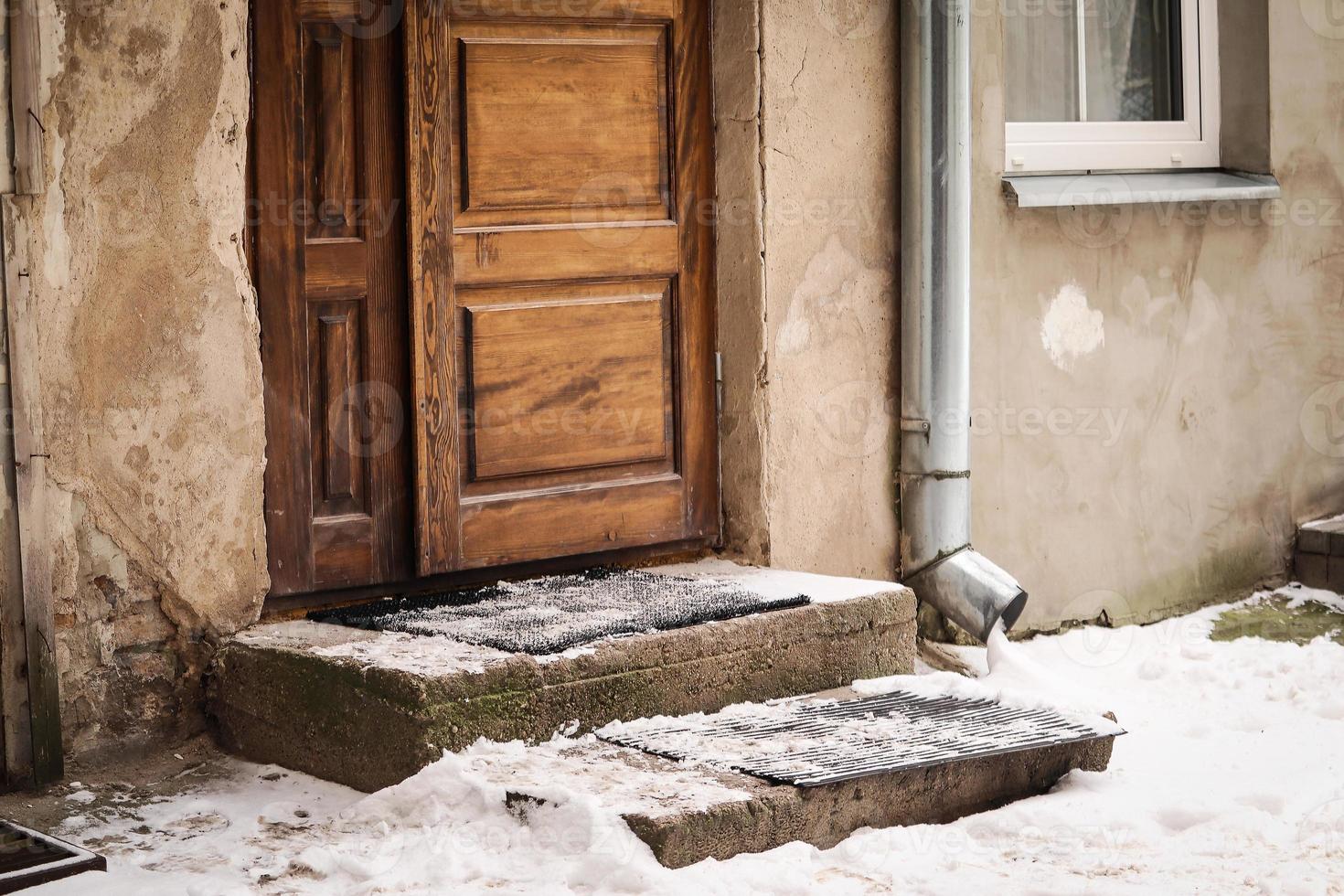 Old wooden door and thick pack of snow on the doorstep of a residential buildong near a water pipe in old town photo