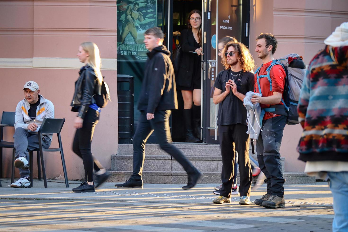 Vilnius, Lithuania. June 06 2022 - Two male friends standing together in the street listening to music while other people passing by photo