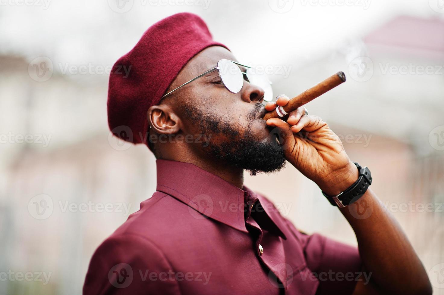 Portrait of African American military man in red uniform, sungalasses and beret. Captain smoke cigar. photo