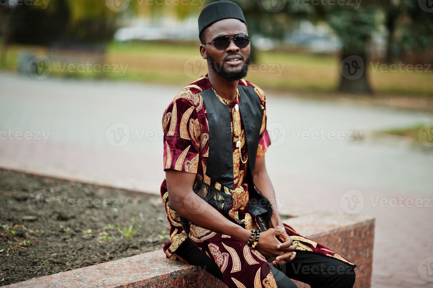 African stylish and handsome man in traditional outfit and black cap standing outdoor. photo