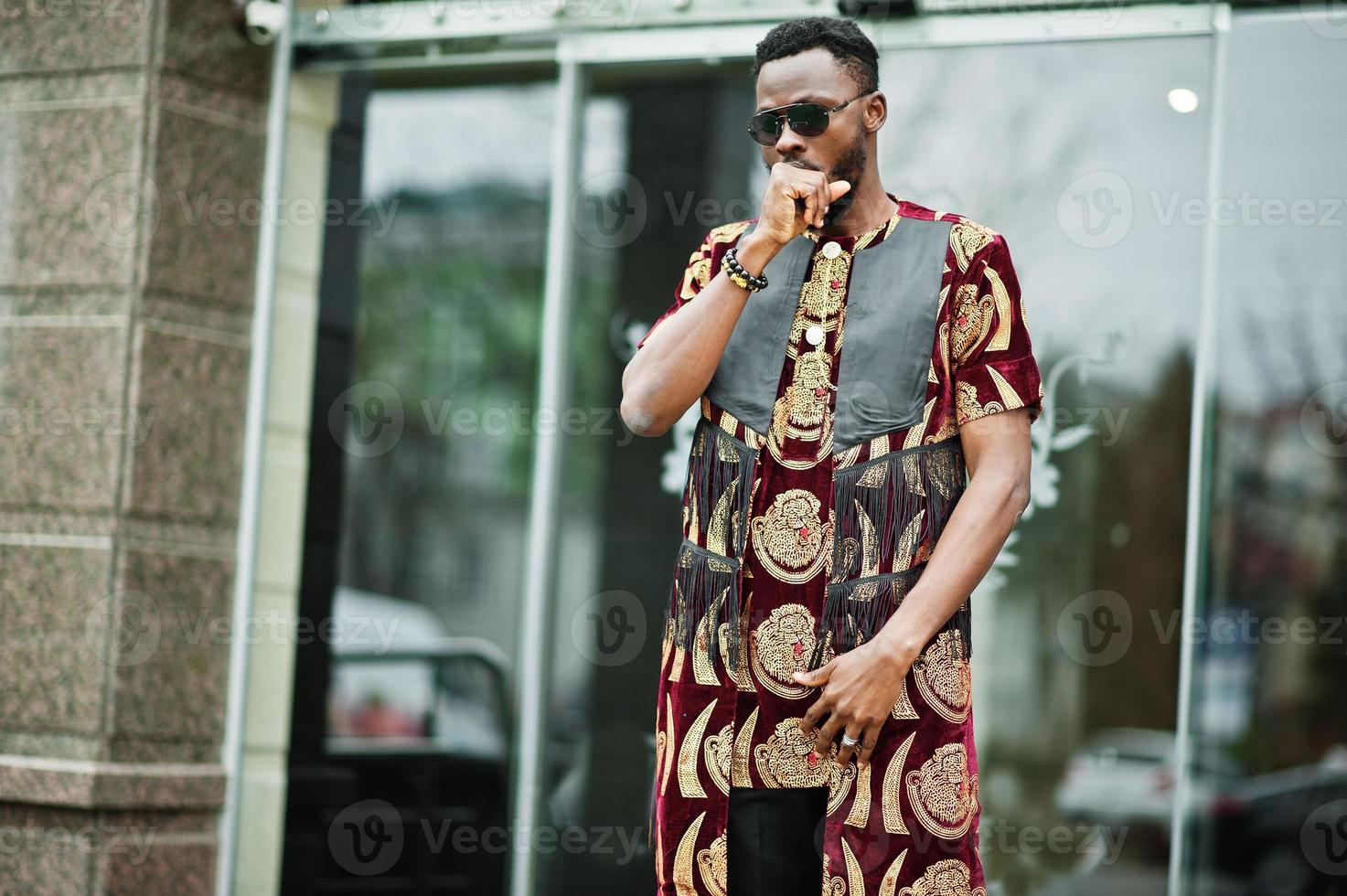 African stylish and handsome man in traditional outfit and sunglasses standing outdoor. photo