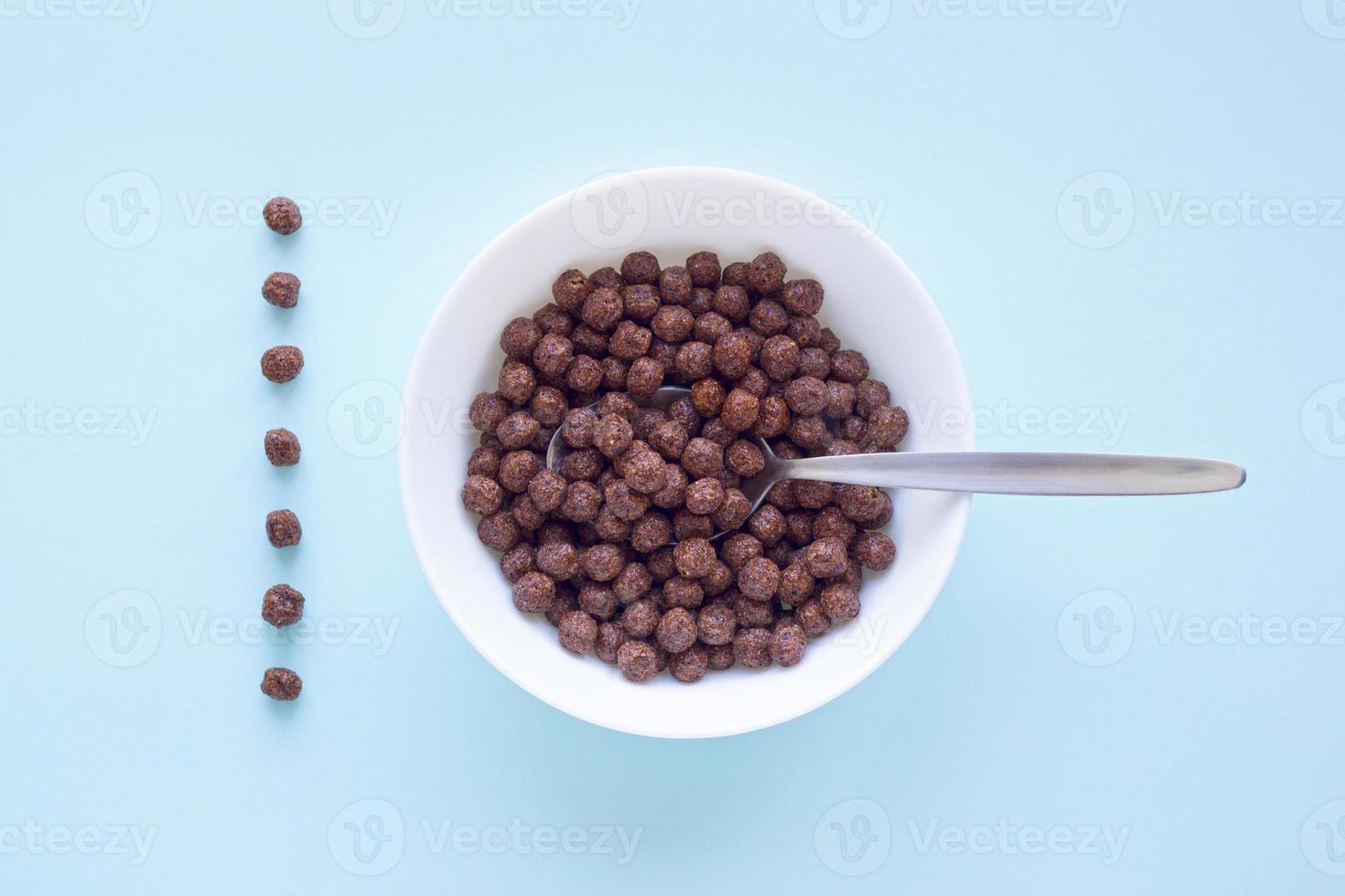 Chocolate cereal balls in white bowl on blue background. Dry breakfast cereal top view. Concept for a healthy diet photo