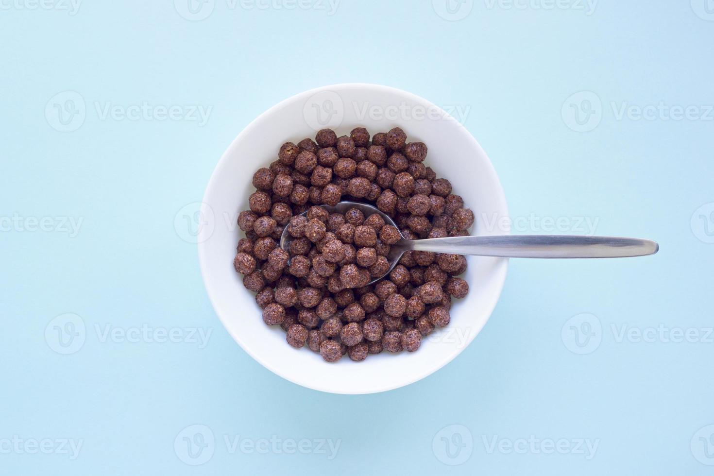 Chocolate cereal balls in white bowl on blue background. Dry breakfast cereal top view. Concept for a healthy diet photo