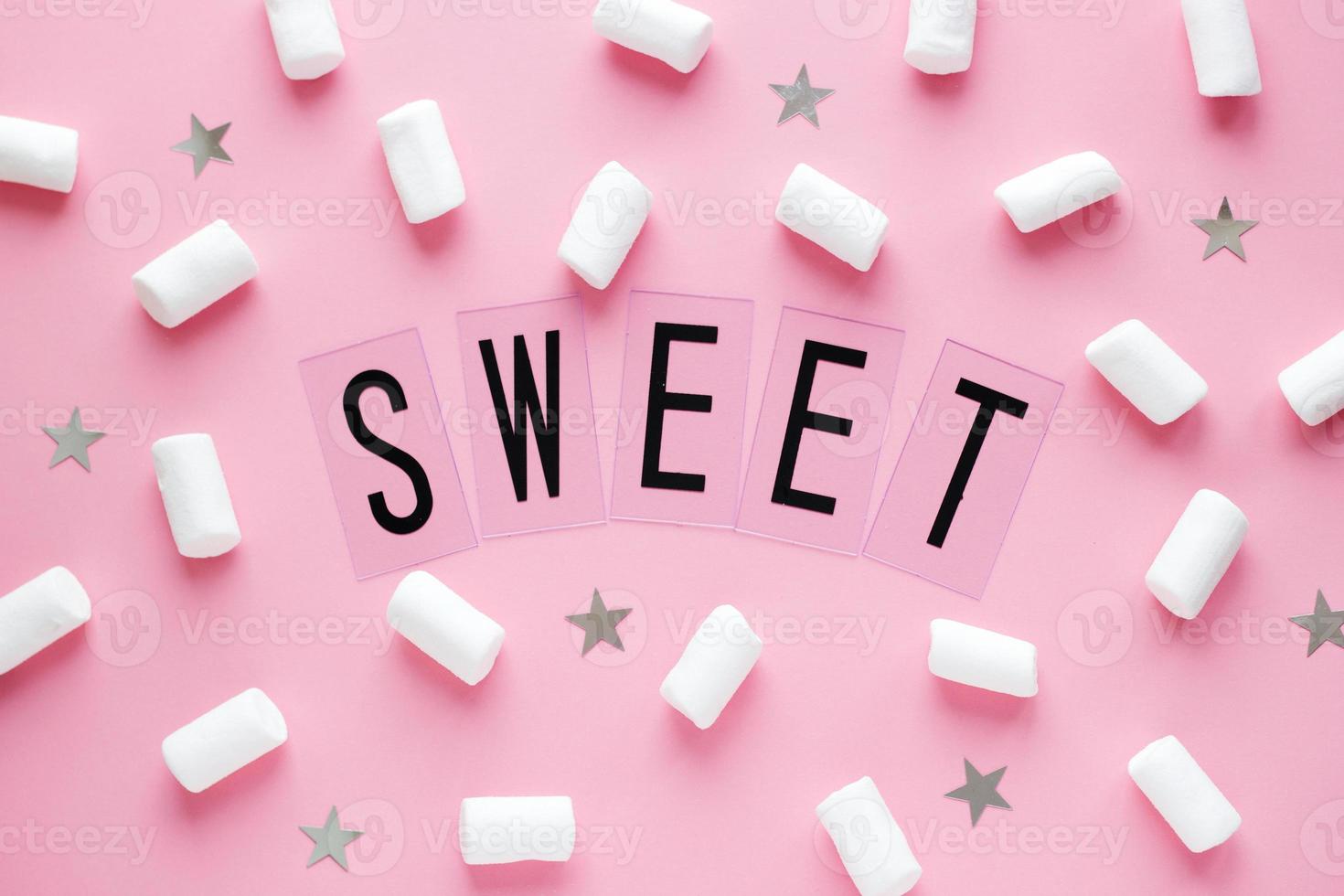 White marshmallows and stars with SWEET word on pink pastel background. Food concept in minimal flatlay style photo