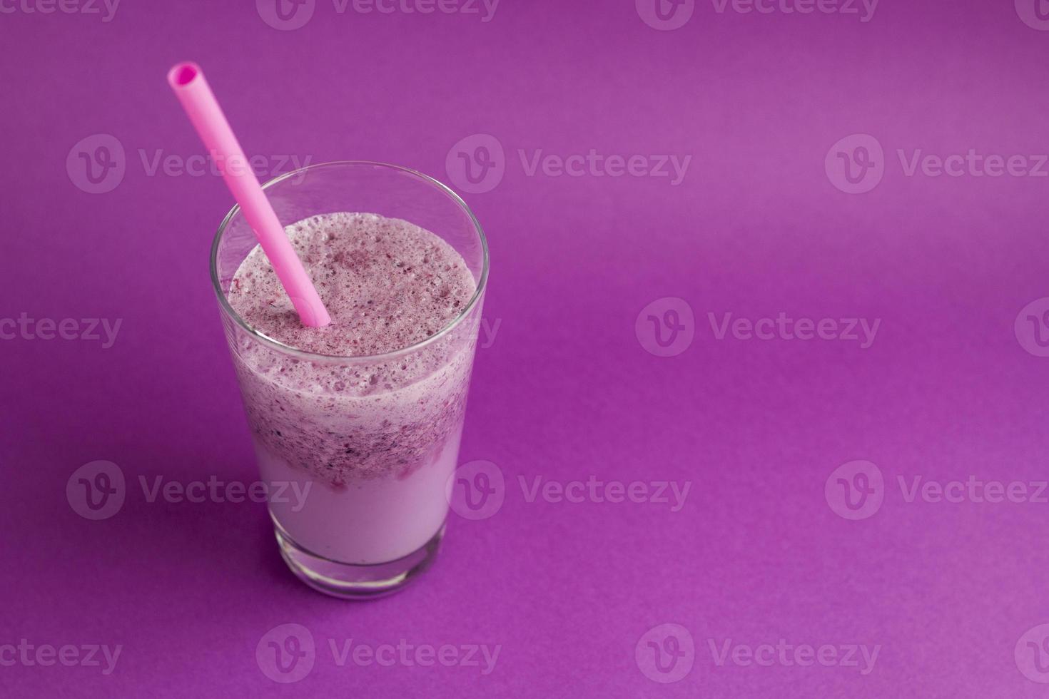 Glass of berry smoothie with straw on purple background. Pink milkshake with copy space. Healthy drink. Blueberry cocktail photo