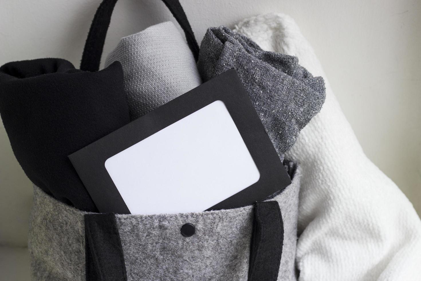 Close-up blank frame and rolled clothes in woolen gray bag on white background. Black, grey and white textiles. Monochrome concept. Copy space for text photo