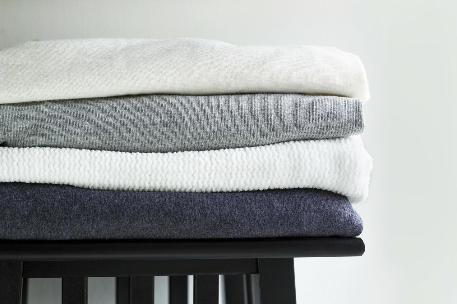 Close-up stack of folded monochrome clothes on white background wall. Black, grey and white textiles clothing on wooden shelf photo