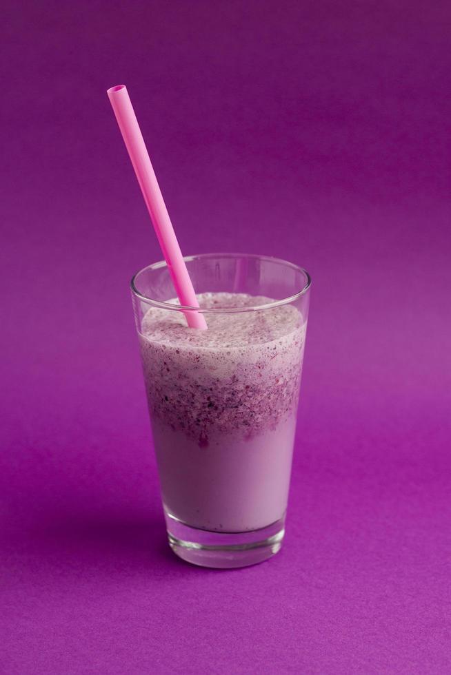 Glass of berry smoothie with straw on purple background. Pink milkshake. Healthy drink. Blueberry cocktail photo