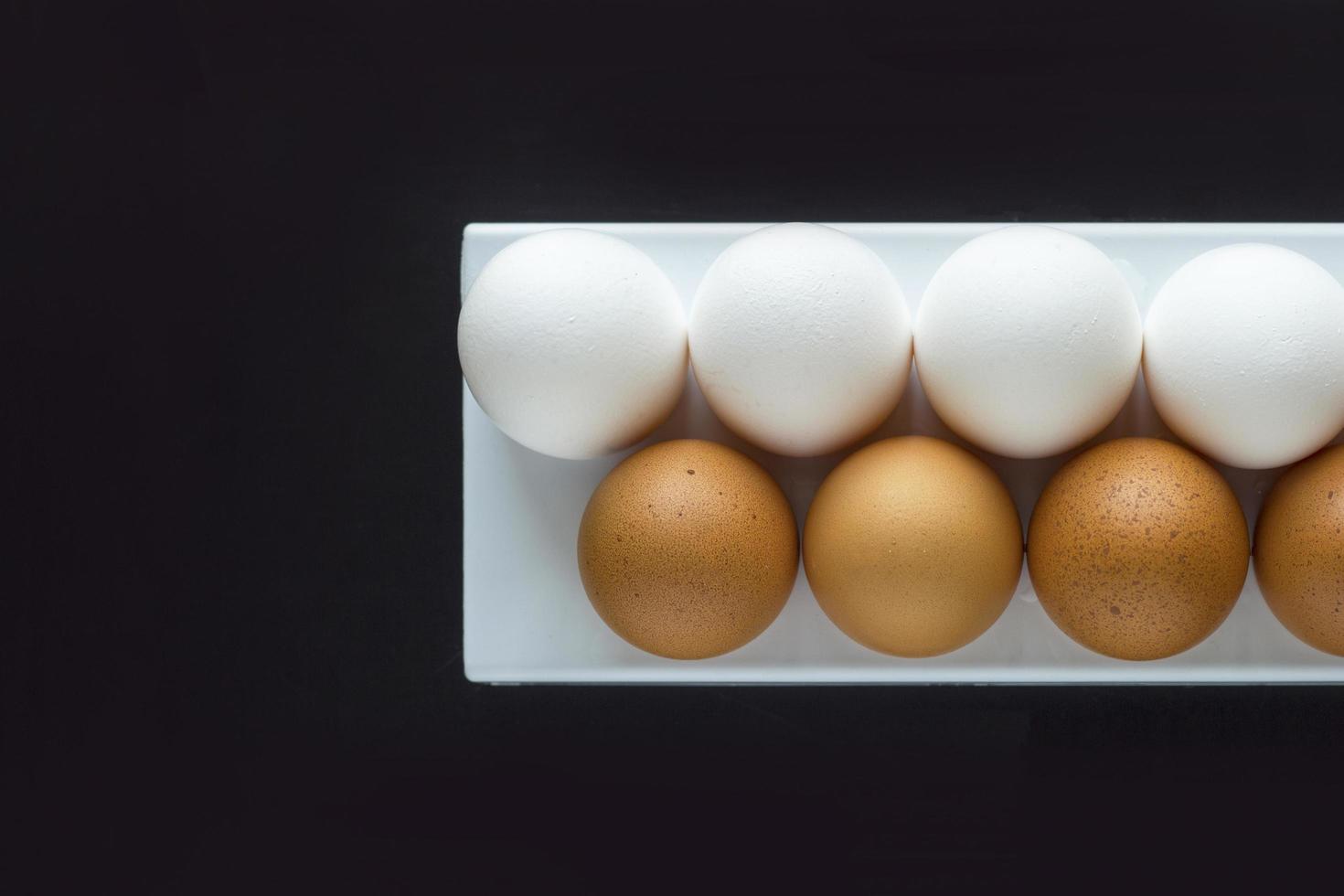 Fresh chicken egg in container on black paper background. Concept for Easter with copy space. White and brown eggs. Top view photo