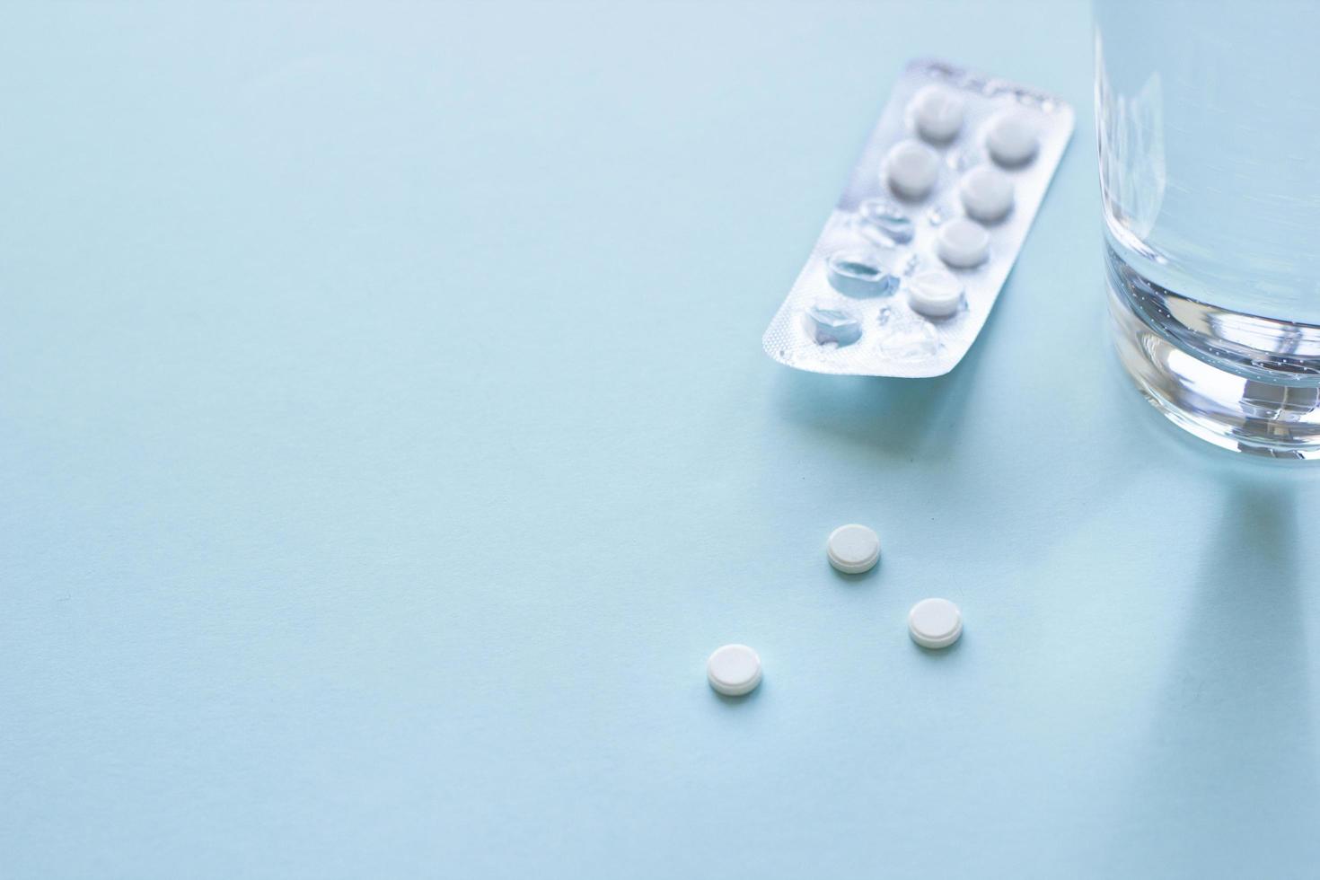 Tablets in blister pack and glass of water on blue background. Healthcare and medical concept with copy space. Top view photo