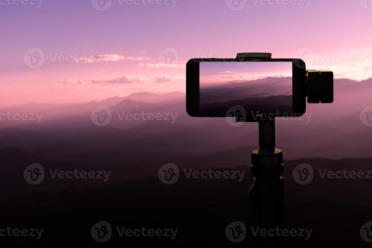 Traveler using smartphone on tripod taking a photo in sunset at the mountains natural background.