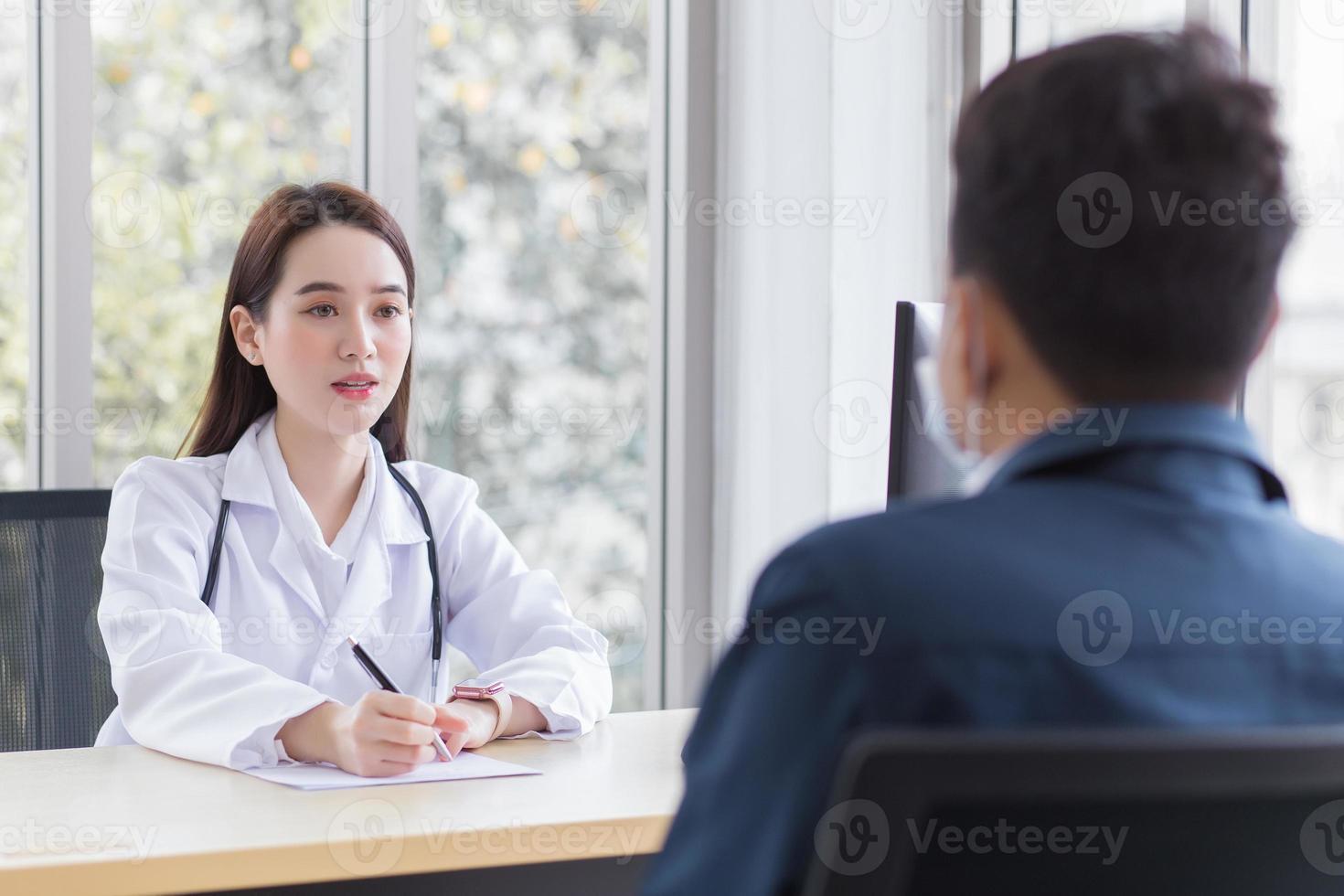 Asian professional woman doctor who wears medical coat talks with a man patient to consult and suggest healthcare information to him at the examination room in the hospital. photo