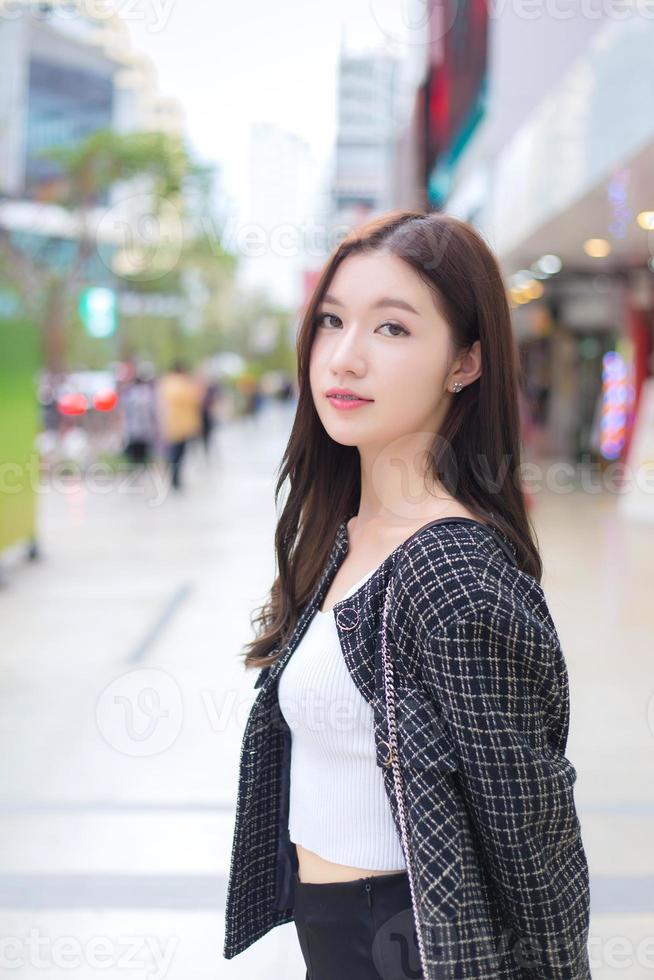 Portrait of a beautiful, long-haired Asian female in a black pattern coat with braces on teeth walking and smiling outdoors in the city. photo