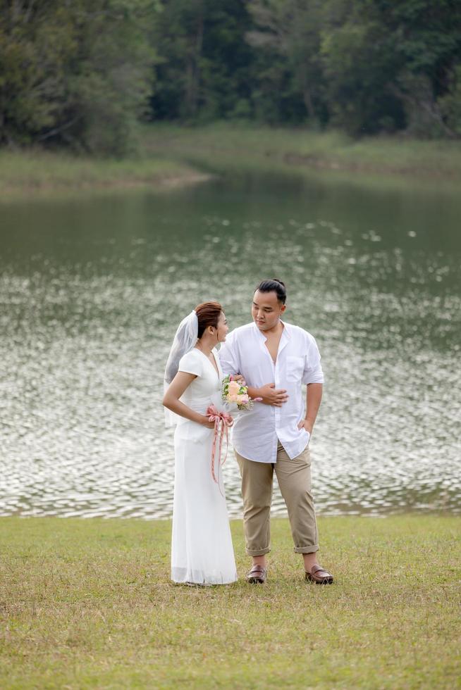 The bride and groom are taking pictures in the beautiful natural forest wearing white dresses. photo