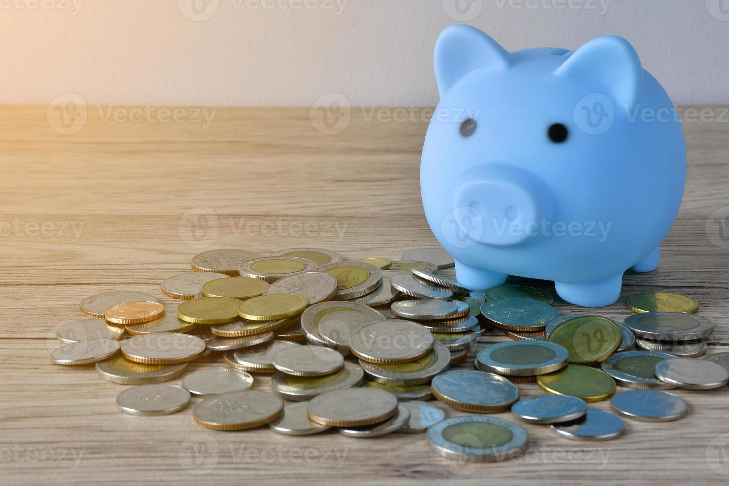 A blue piggy bank on a  pile of coins on wooden table to save money. photo