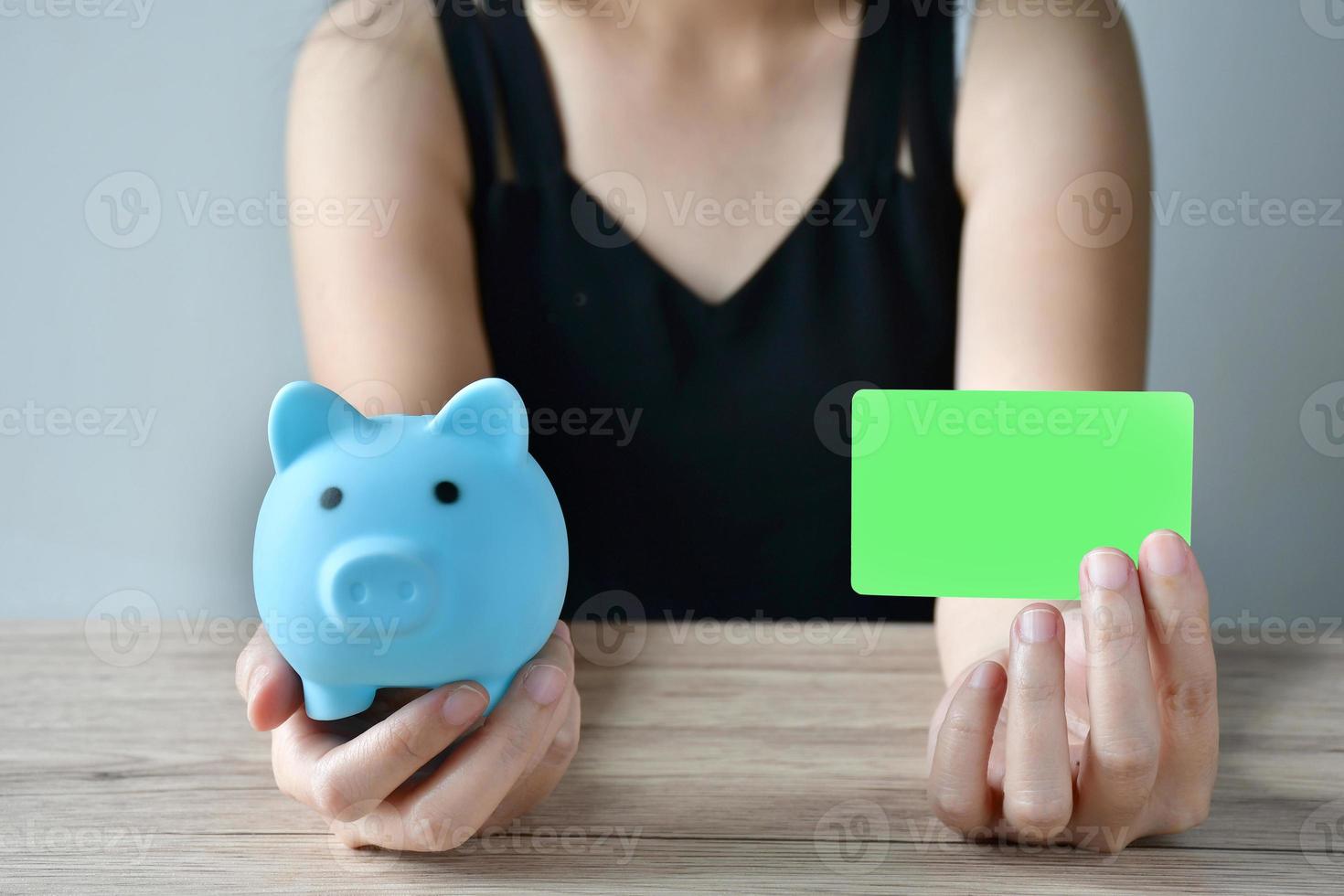 A girl with a pig blue piggy bank and a white credit card mock up to choose how to use the money for shopping. photo