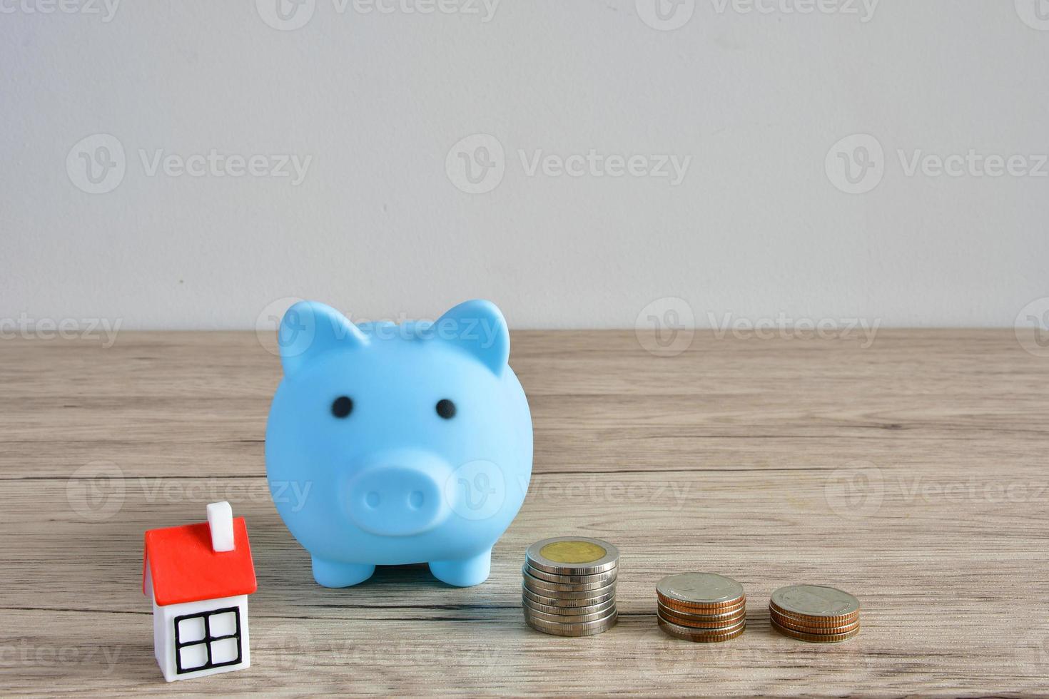 A stack of coins and blue piggy bank on the wooden table to save money for buying a house. photo