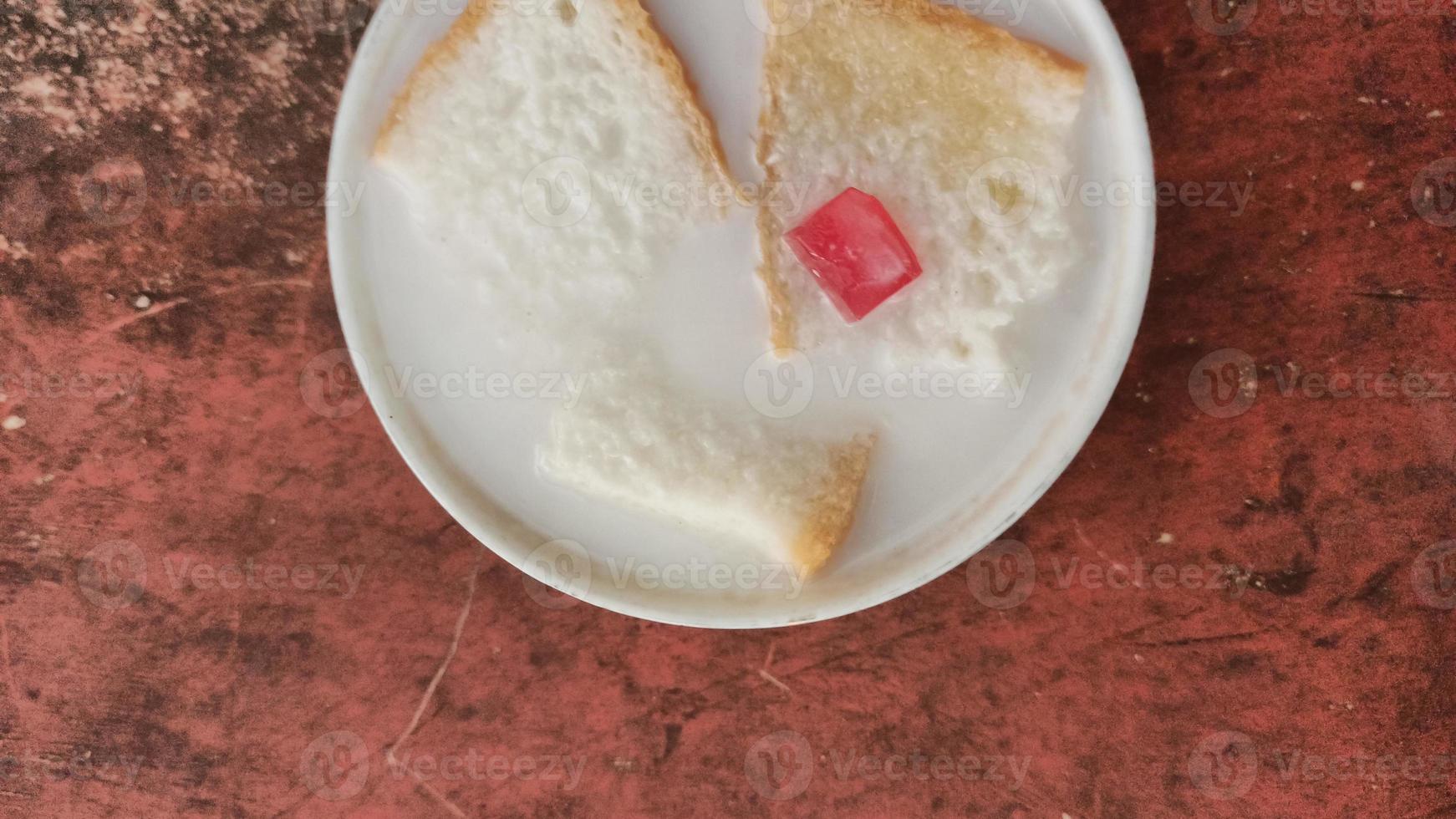 wedang asle comida servida en un tazón lleno de leche mezclada con arroz pegajoso y unas rebanadas pequeñas de pan blanco foto