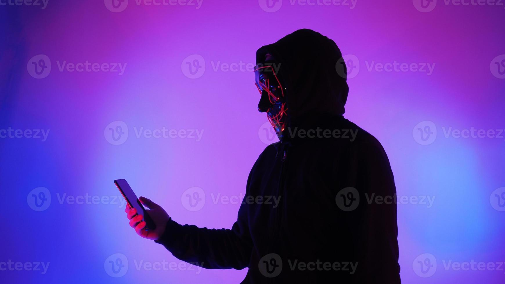 Anonymous hacker and face mask with smartphone in hand. photo