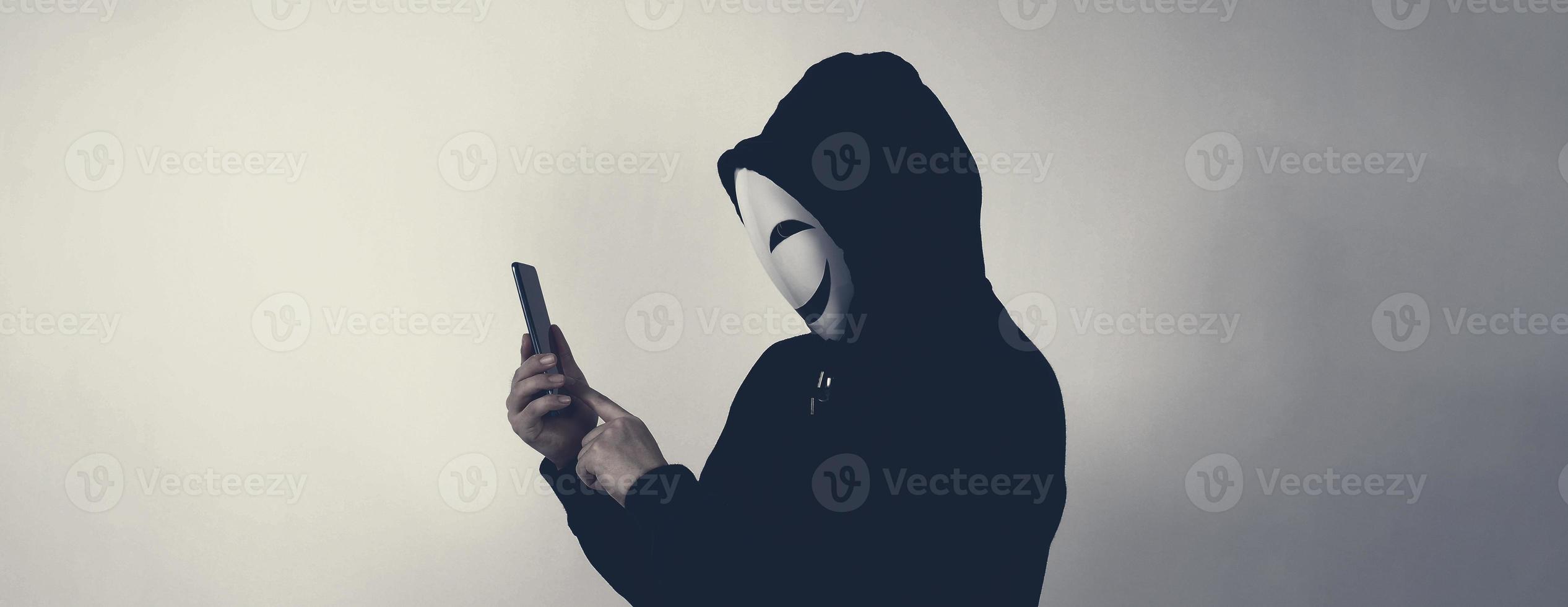 Anonymous hacker and face mask with smartphone in hand. photo