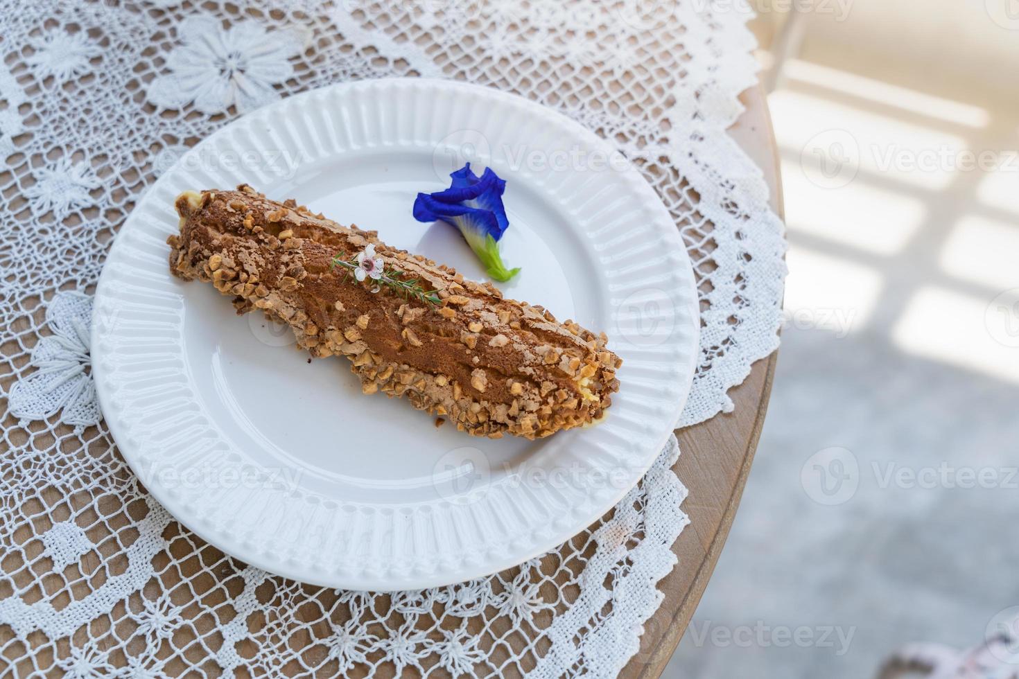 Homemade puff pastry deep fried Eclairs with vanilla cream topping with almonds nut on white plate over table top with lace tablecloth. traditional french dessert. selective focus photo