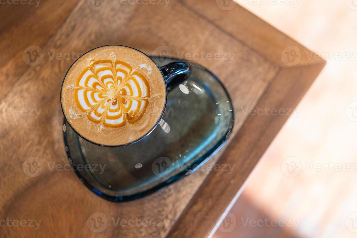 top view of coffee latte cup in coffee shop. hot macchiato coffee with caramel arts in black mug on wooden table in cafe with copy space and sunlight background photo