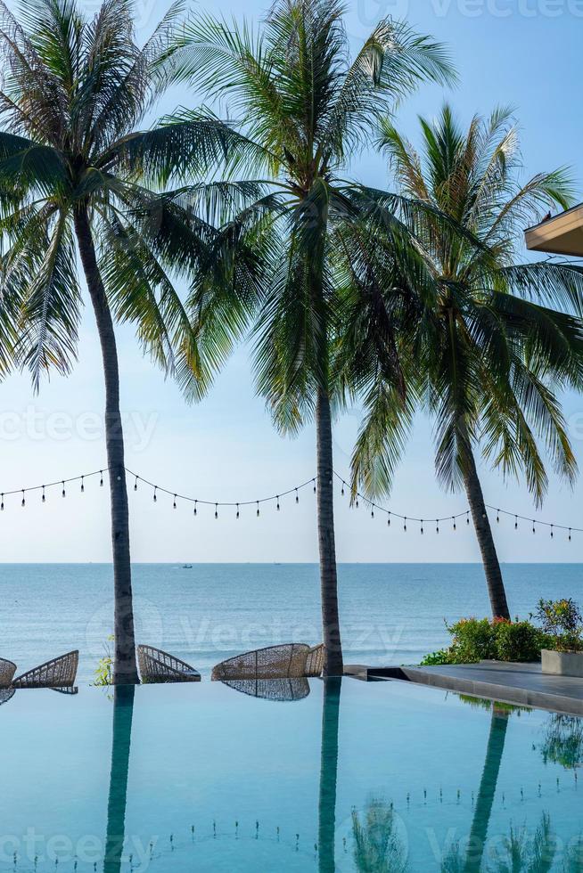 Beautiful tropical beach and sea with palm tree, coconut tree and chair around swimming pool in hotel resort for travel and vacation. relaxing summer in infinity swimming pool looking at view. photo
