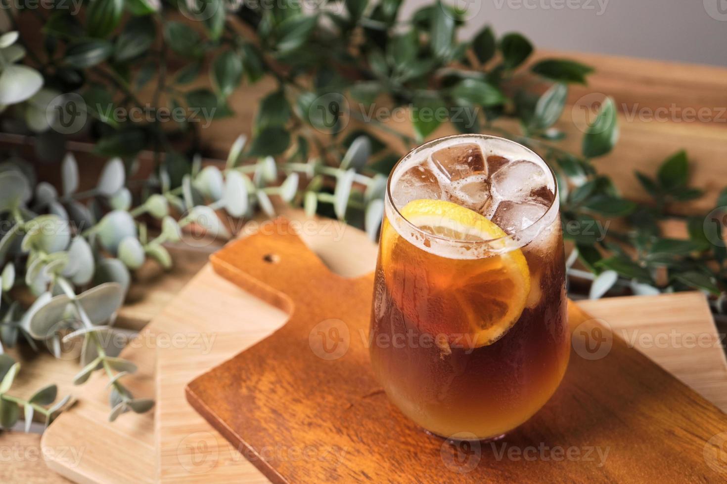 cold iced black brew coffee mixed lemon juice and lemon slices in a glass with pieces of ice on a wooden table, natural light, fresh summer drink in the morning photo