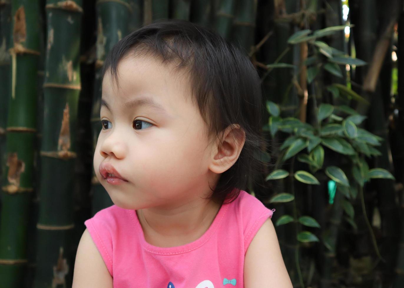 Encantadora niña asiática de 3 años con camiseta rosa mirando hacia un lado. foto