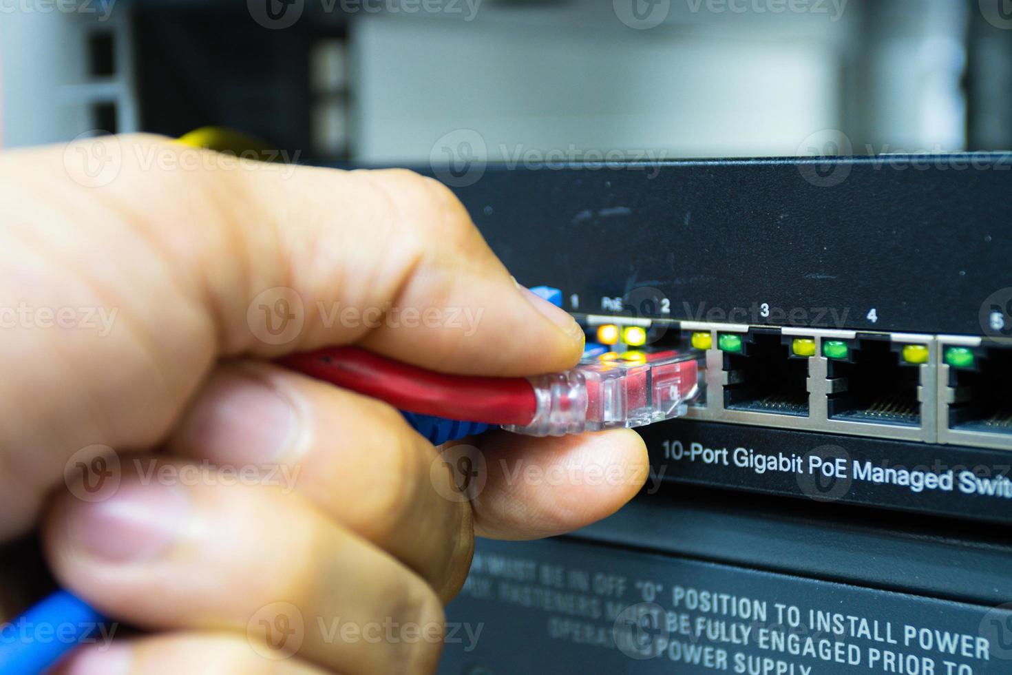 mano de un hombre que sostiene los cables de red para conectar el puerto de un conmutador para conectar la red de Internet, tecnología de comunicación conceptual foto