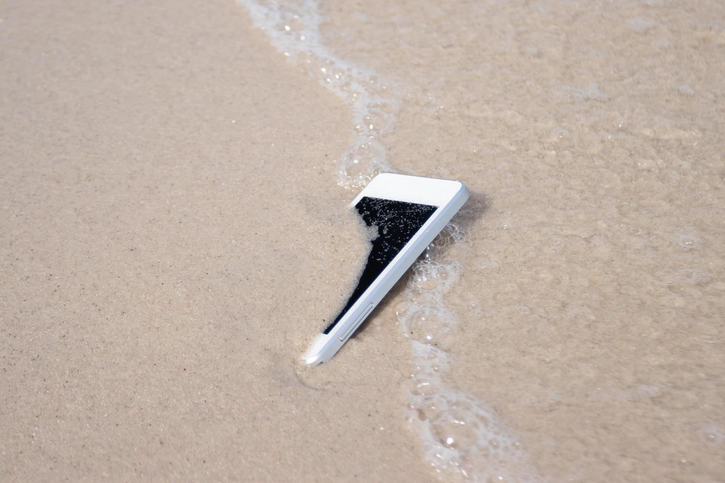 teléfono móvil blanco sobre la arena en la playa concepto de residuos electrónicos foto