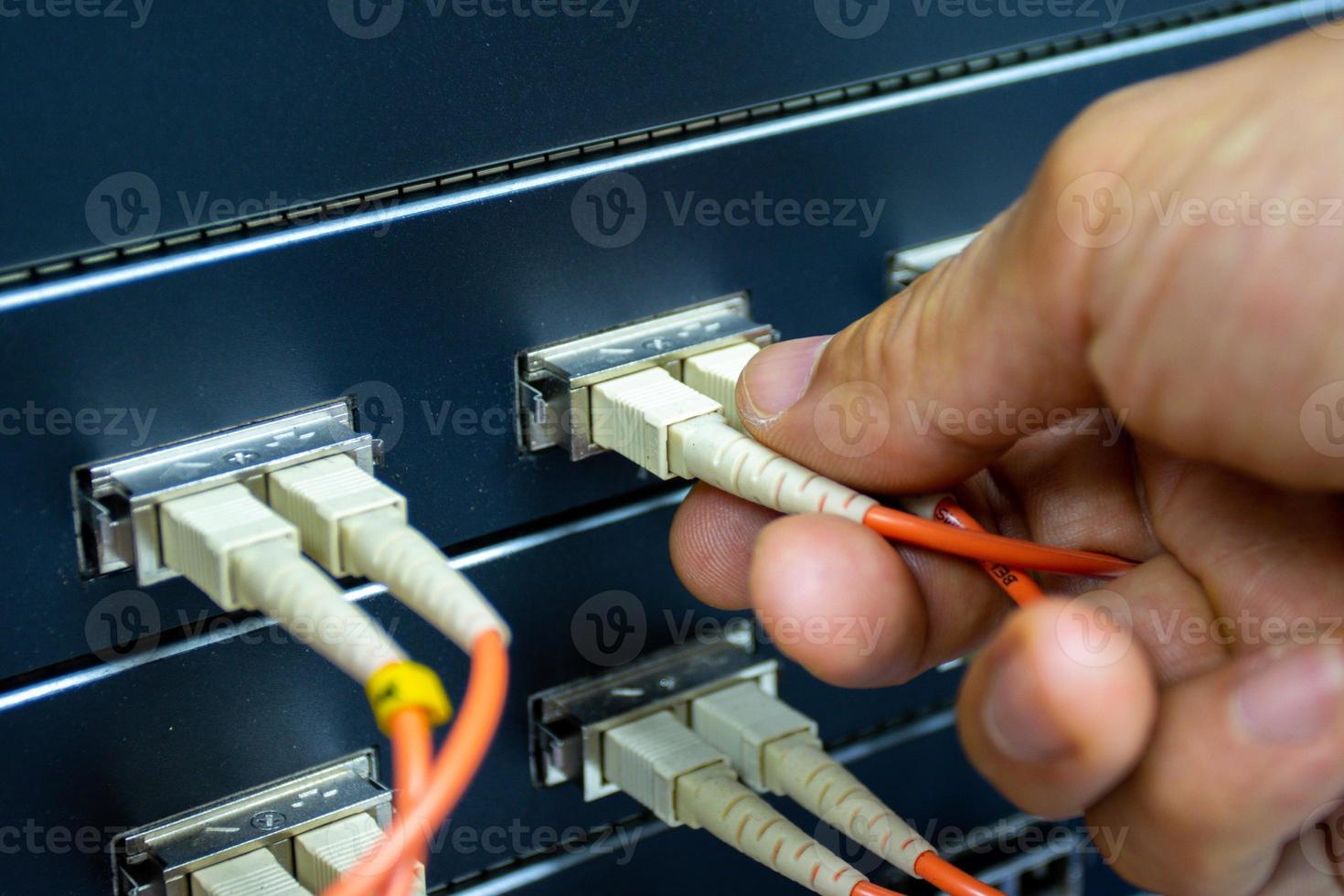 mano de un hombre que sostiene los cables de fibra óptica de la red para conectar el puerto de un interruptor para conectar la red de Internet, tecnología de comunicación conceptual foto