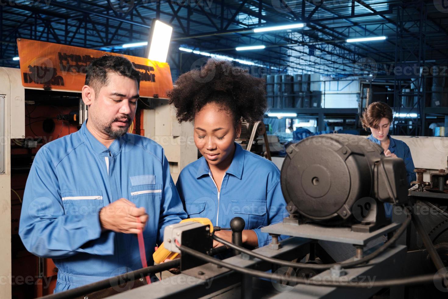 Asian male and female African American engineers in safety uniform work by inspecting machines' voltage current, checking, and maintaining at manufacture factory, electric system service occupations. photo