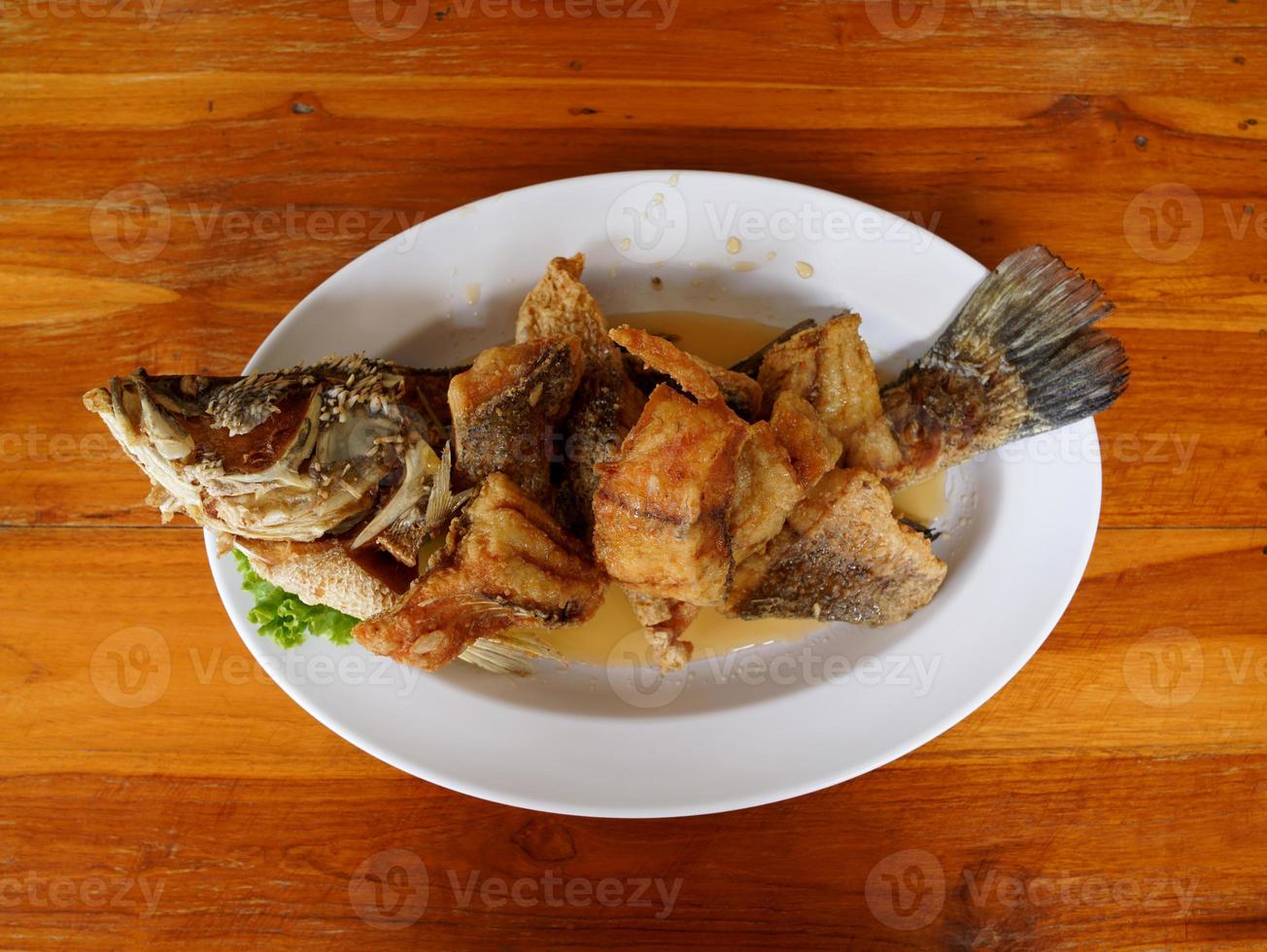 deep-fried snapper fish topped with fish sauce on white dish on wooden table photo