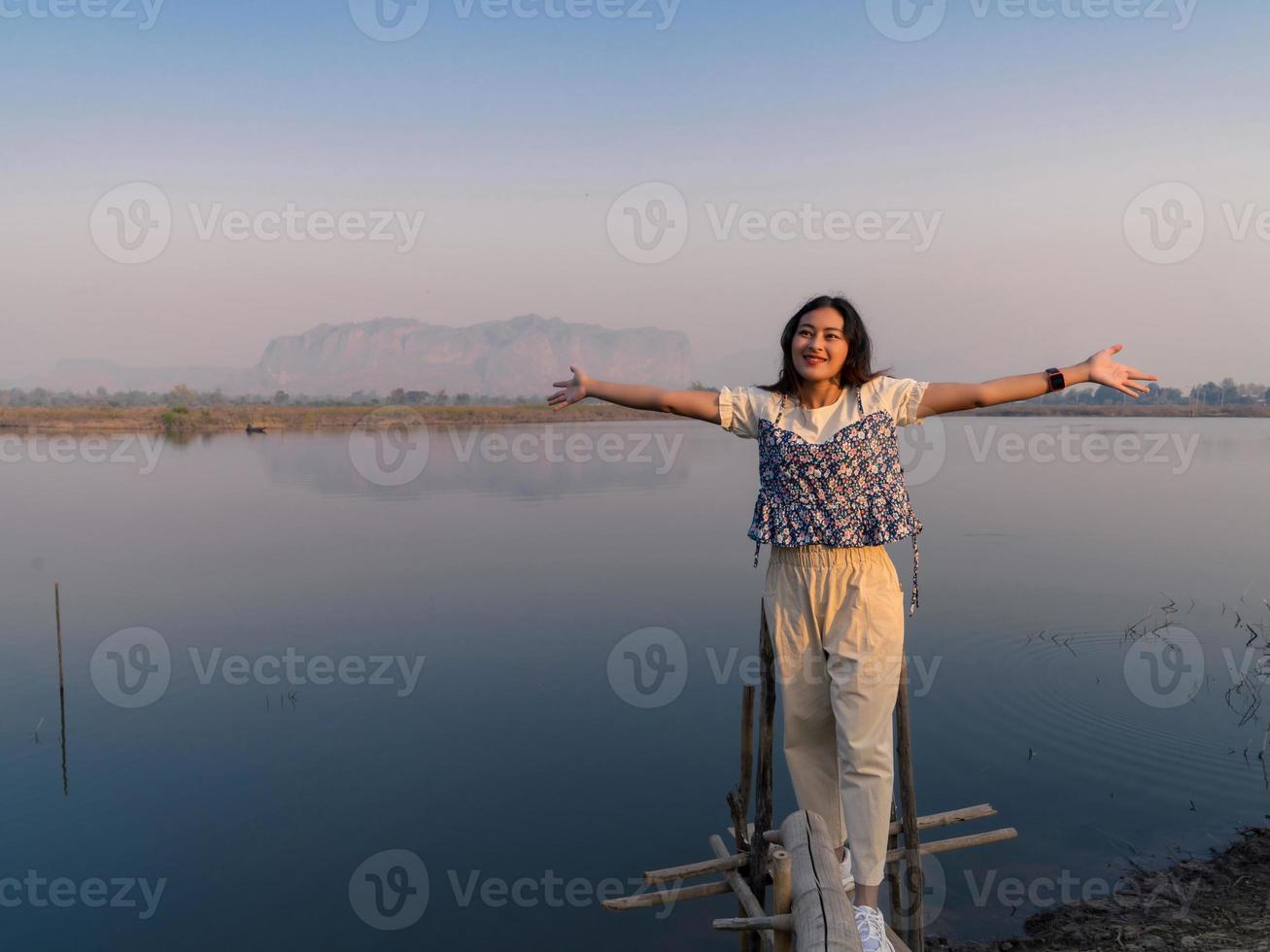 smile happy Asian woman tourist standing freedom arms open at beautiful calm mountain landscape with front lake reflection photo