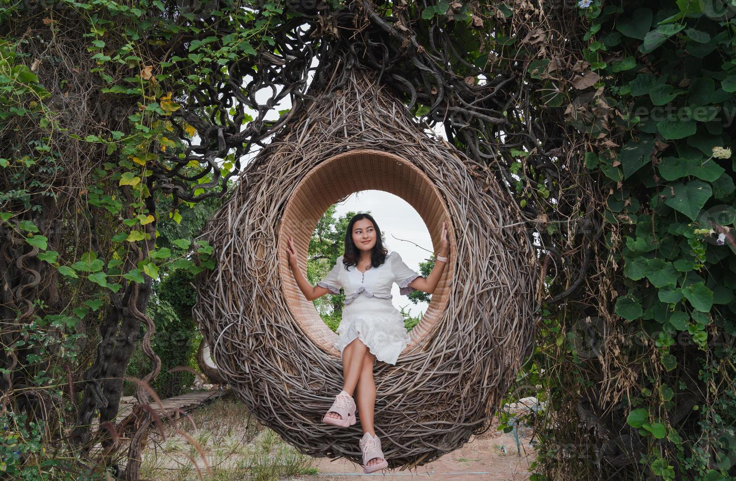 Asian woman sitting in wooden bird nest in green tree forest looking away at nature photo
