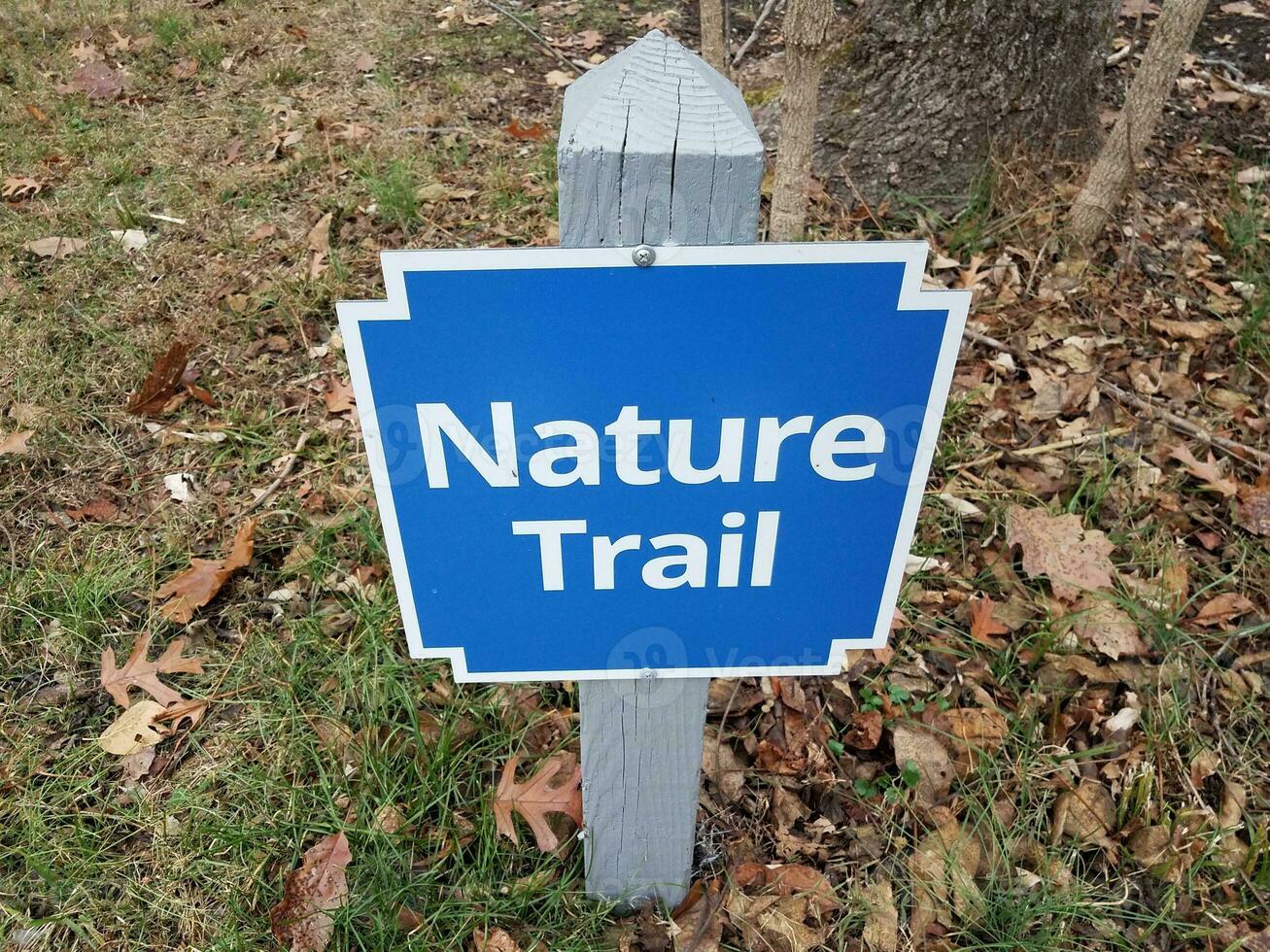 blue nature trail sign on stake with leaves and grass photo